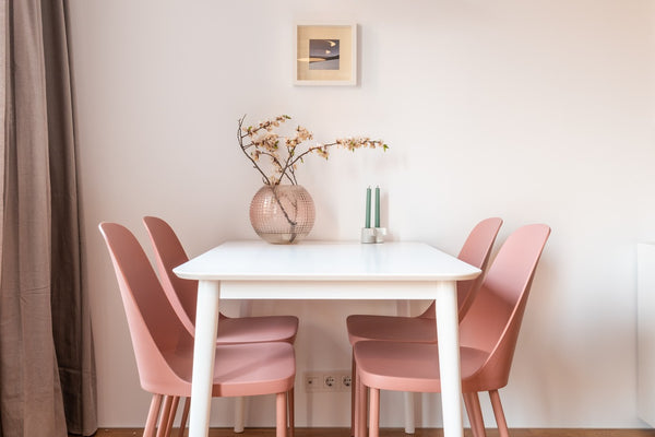 4 roze stoelen aan een witte eettafel